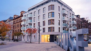 foto zeigt neubau gebäude vorderanasicht und vor dem haus einen künstlerischen schriftzug zuhause