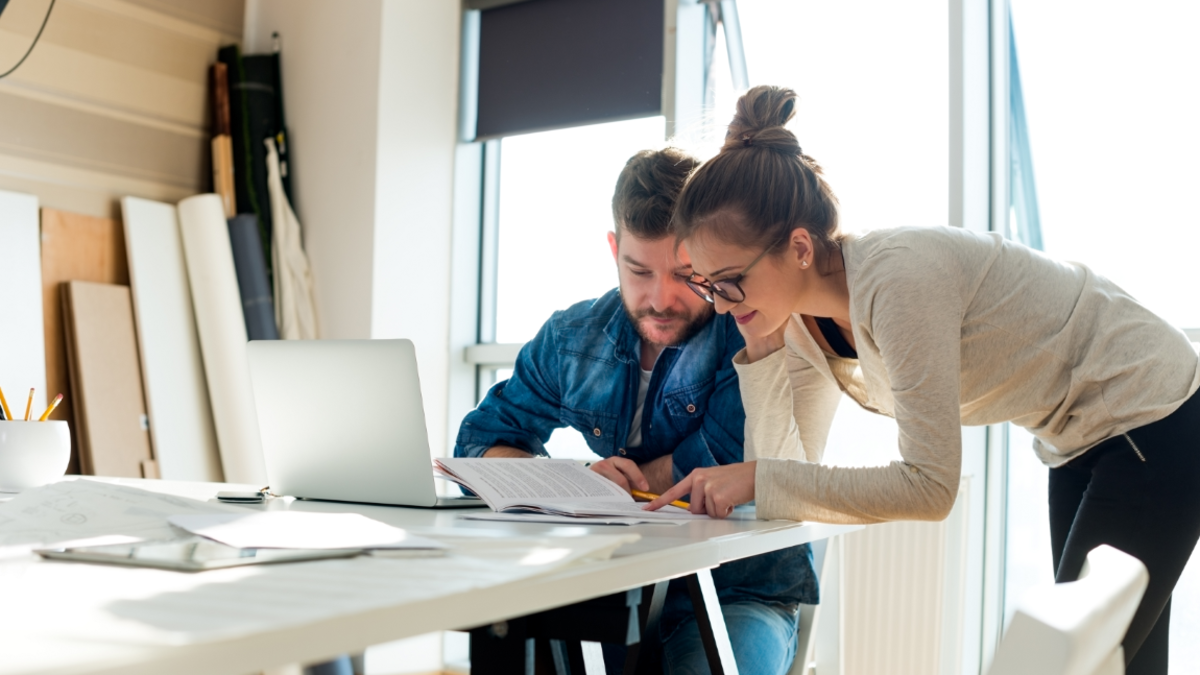 foto zeigt einen mann und eine frau die sich an einem beratungstisch über einen laptop beugen