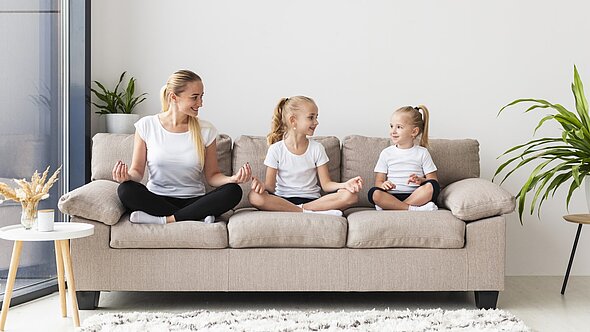 foto zeigt frau mit zwei töchtern auf couch sitzend