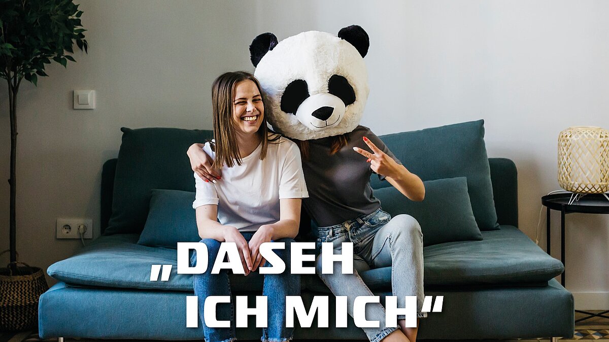 foto zeigt eine frau auf einer couch sitzend neben einer als pandabär verkleideten person